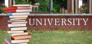 a pile of books stacked in front of a brick sign that says "university"